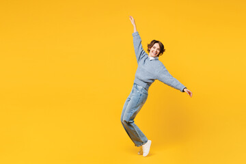Full body side view young woman wear grey knitted sweater shirt casual clothes leaning back with outstretched hands stand on toes fooling around isolated on plain yellow background. Lifestyle concept
