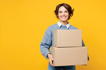 Young smiling happy cheerful woman she wears grey knitted sweater shirt casual clothes hold cardboard boxes looking camera isolated on plain yellow color background studio portrait. Lifestyle concept.