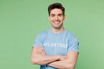 Young happy man wear blue t-shirt white title volunteer look camera hold hands crossed folded...