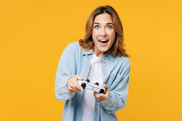 Young gambling excited woman she wears blue shirt white t-shirt casual clothes hold in hand play pc game with joystick console isolated on plain yellow background studio portrait. Lifestyle concept. - obrazy, fototapety, plakaty