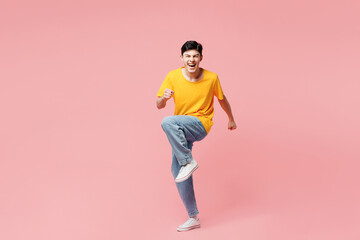 Full body young fun man he wears yellow t-shirt casual clothes doing winner gesture celebrate clenching fists say yes isolated on plain pastel light pink background studio portrait. Lifestyle concept.