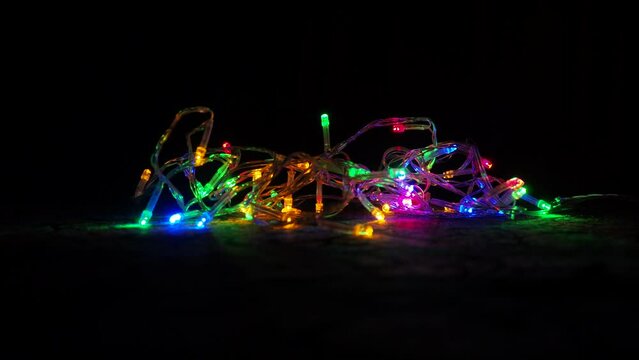flashing multi-colored blurry lights of garlands lying on the surface. New Year background, Christmas Xmas. Floating focus in dark. Festive room illumination and design. Red green blue yellow bulbs