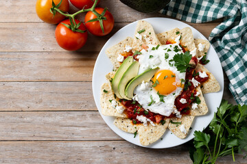 Traditional Mexican breakfast red chilaquiles with egg on wooden table. Top view. Copy space