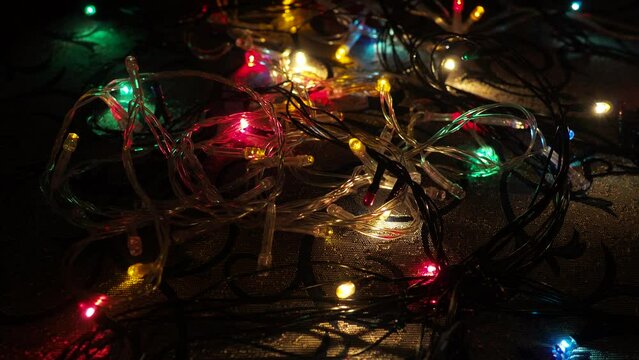 flashing multi-colored blurry lights of garlands lying on the surface. New Year background, Christmas Xmas. Floating focus in dark. Festive room illumination and design. Red green blue yellow bulbs