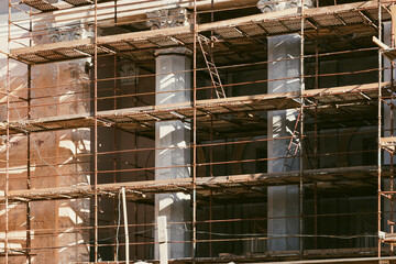 Reconstruction of building facade. Renovation of an old historic construction with columns, bas-relief stucco and decorative details. Scaffolding. Industrial concept. Municipal service.