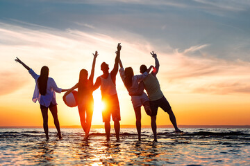 Five happy young friends are having fun, standing together, hugging and meeting sunset with open arms at calm sunset lake beach