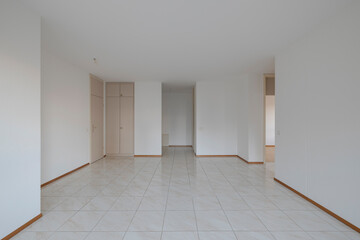 Front view of a very bright living room with white walls. In the background you can see a built-in wardrobe and the entrance to the apartment.