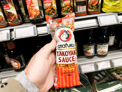 Berlin, Germany - Jan 25, 2024: POV of a male shopping for Asian food inside the supermarket, holding a package of Otafuku takoyaki sauce for topping ready to taste new cuisines