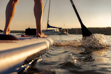 Close up photo of man surfer legs is standing on stand up paddle sup board at sunset calm lake