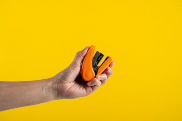 Orange stapler in hand isolated on yellow background
 - obrazy, fototapety, plakaty
