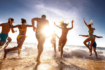 Large group of happy young tourists are having fun, runs and jumps at sunset sea beach. Tropical holidays concept