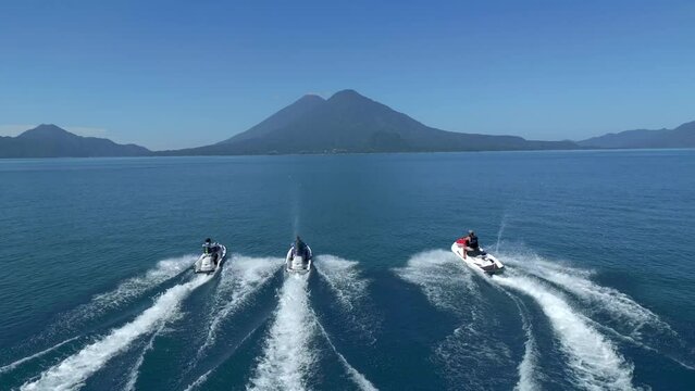 Three Young Men Jet Skiing Towards Atitlan Lake Volcanoes, Guatemala. Tracking Drone Shot