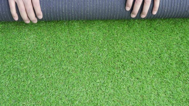 Men's hands holding a roll of artificial grass and installing it on a house. Artificial grass background.