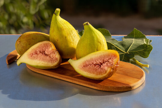 Whole figs and one fig sliced in half. On small cutting board. Ripe green fig fruits on table in garden. Close-up
