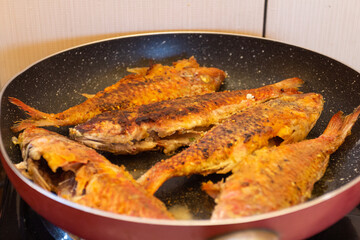 Fried fish in a frying pan on a gas stove in the kitchen