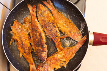 Fried fish in a frying pan on a gas stove in the kitchen