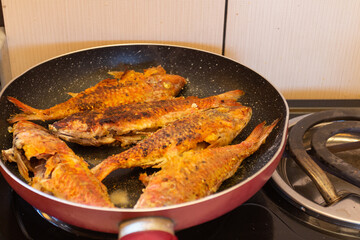 Fried fish in a frying pan on a gas stove in the kitchen