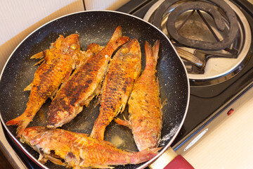 Fried fish in a frying pan on a gas stove in the kitchen