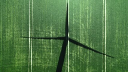 Shadow of a large wind generator on the green grass. Blades of the wind turbine are slowly rotating. Aerial view from above. Environmental protection, renewable energy sources. 4k footage