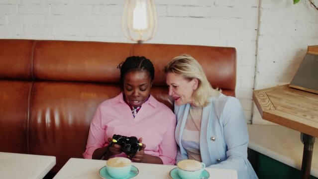 Two attractive women sitting in cafe and looking at photos taken on cameraTwo attractive women sitting in cafe and looking at photos taken on camera