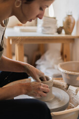 Close-up of a focused artist molding a clay pot on a spinning pottery wheel.