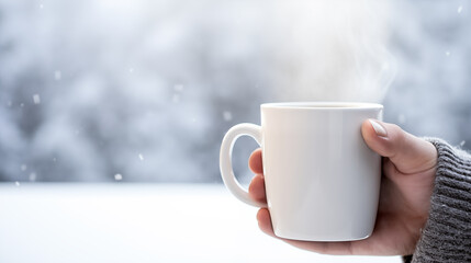 Close-up of a person holding a steaming mug against a snowy backdrop, snowflakes visible in the air