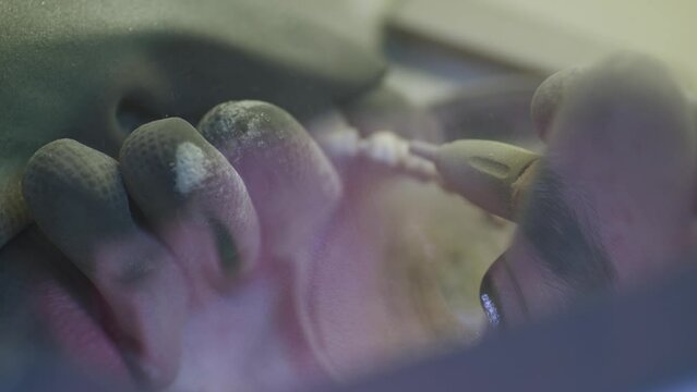 A man's reflection in the glass. Close up. Dental technician polishing artificial ceramic teeth using sandblaster in the dental lab.
