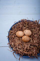 Beautiful brown painted Easter eggs in nest on blue background. Natural tea coloring for Easter eggs. Top view, copy space, vertical shot