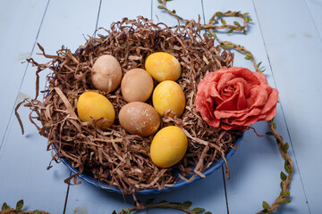 Decorative nest with painted Easter eggs and fabric rose flower on blue wooden background. Yellow and brown eggs for Easter, close up
