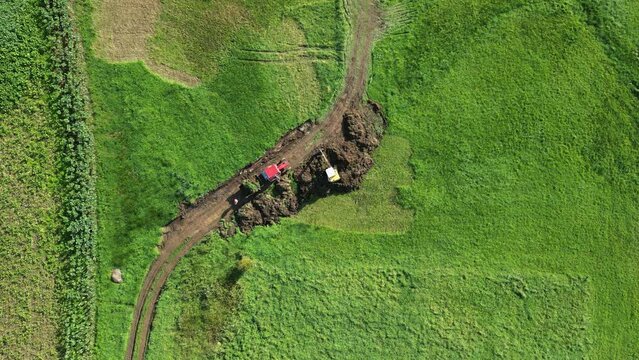Top down drone footage of a backhoe loader excavating soil in a green field in Zas, A Coruna, Spain