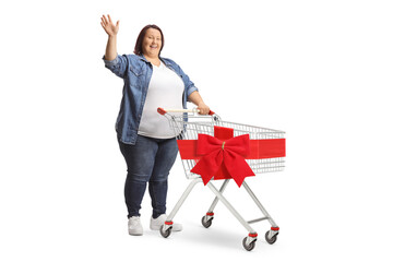 Corpulent woman waving and standing with a shopping cart