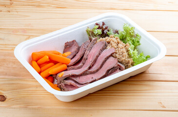 Veal sous vide with juicy carrots. Healthy diet. Takeaway food. Eco packaging. On a wooden background.