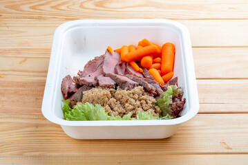 Veal sous vide with juicy carrots. Healthy diet. Takeaway food. Eco packaging. On a wooden background.