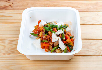 Sautéed vegetables. Healthy diet. Takeaway food. Ecological packaging. On a wooden background.