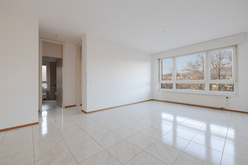 Empty living room with large bright window with a radiator underneath.