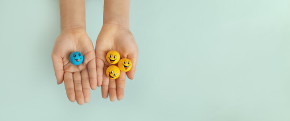 three yellow smiley faces in one hand and one blue smiley face in other child's hand on blue background, copy space