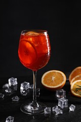 Glass of tasty Aperol spritz cocktail with orange slices and ice cubes on table against black...