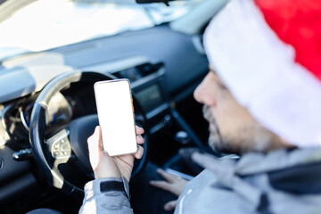 Man sitting on driver seat and holding blank screen mobile phone. Christmas travel and transportation concept.