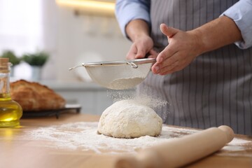 Making bread. Man sprinkling flour onto dough at wooden table in kitchen, closeup