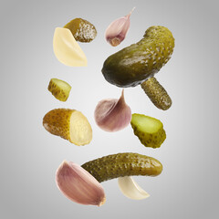 Tasty pickled cucumbers and garlic falling on light grey background