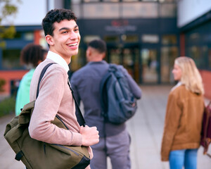 Portrait Of Male University Student Looking Over Shoulder With Friends Outside College Buildings