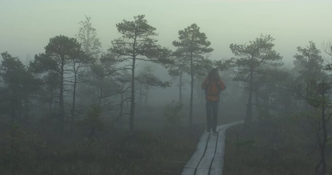 Man with dreadlocks and a backpack walking on a trail in a raised bog in thick fog