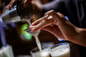 Skilled bartender crafts an exquisite cocktail, expertly pouring liquid from the shaker into the glasses. Unique experience and elegance in every drop.