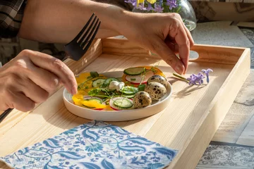 Foto op Canvas Hands of senior woman having breakfast with spring vegetable salad. Salad with quail eggs. In white plate on wooden tray © lassi meony