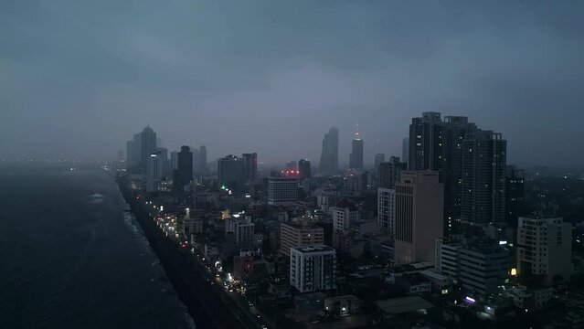 Aerial night view of Colombo skyline glows against dark sea. Urban landscape with illuminated buildings, streets, commercial centers. Sri Lankas capital cityscape attracts tourists, investors.