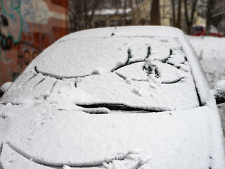 Smiling face drawn on snowy car. Snow on cars after snowfall. Winter scene.