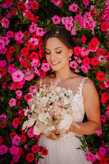 Valmiera, Latvia - July 7, 2023 - Bride with bouquet against a backdrop of pink flowers, looking down, smiling gently...