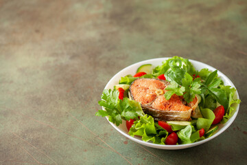 Fresh vegetable salad and baked salmon in a plate on the table. Mediterranean diet concept