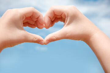 Two hands make a heart shape in the blue sky.