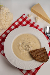 Cauliflower cream soup served in an elegant white plate with wide side, accompanied by a piece of grilled bread on the side. recipe for vegan vegetable soup